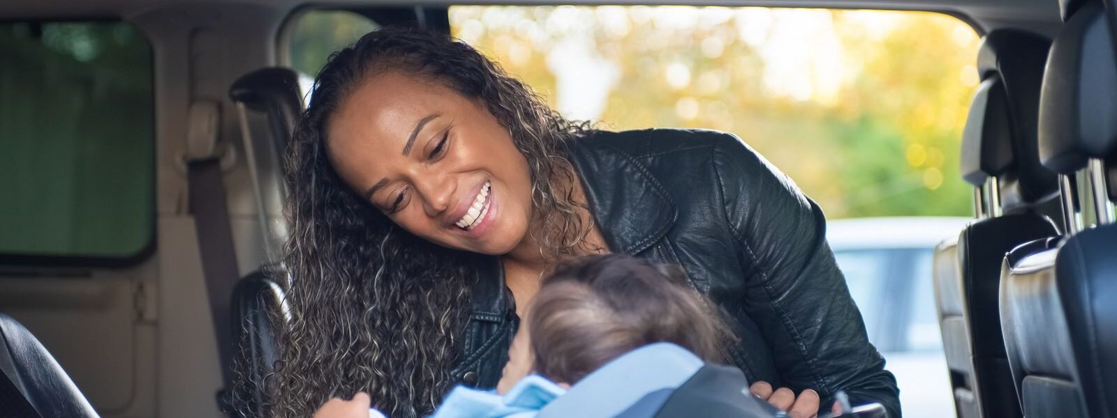 Moeder buigt zich glimlachend over haar baby in een autostoel in de auto