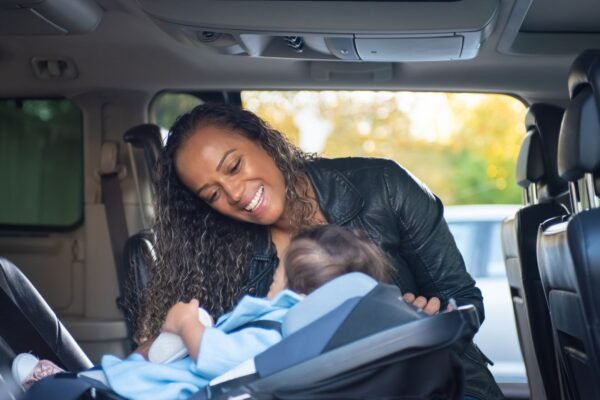 Moeder buigt zich glimlachend over haar baby in een autostoel in de auto