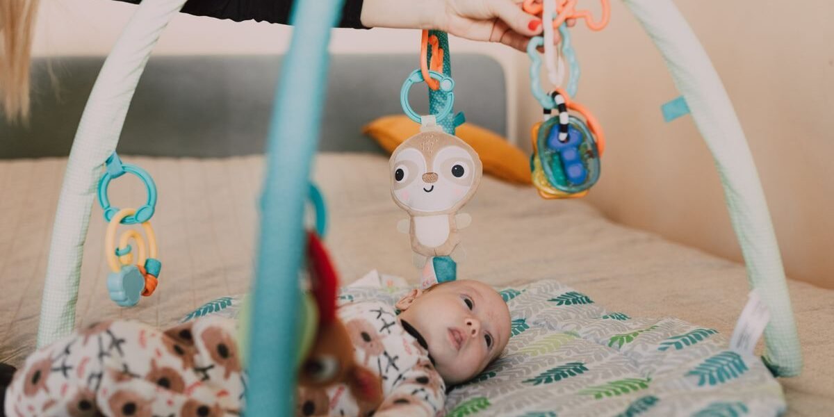Baby van enkele maanden speelt op een speelkleed onder een babygym met kleurrijke hangspeeltjes