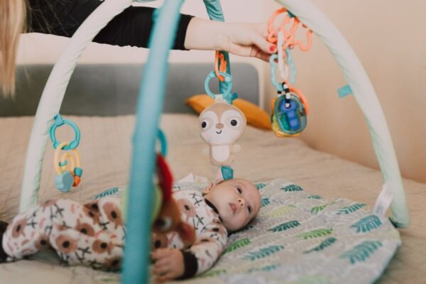 Baby van enkele maanden speelt op een speelkleed onder een babygym met kleurrijke hangspeeltjes