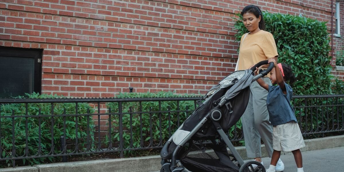 Ouder duwt tandembuggy met baby en peuter door smalle winkelgang