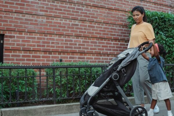 Ouder duwt tandembuggy met baby en peuter door smalle winkelgang