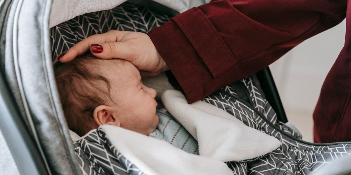 Pasgeboren baby slaapt in een autostoel terwijl een ouder het hoofdje ondersteunt