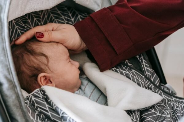 Pasgeboren baby slaapt in een autostoel terwijl een ouder het hoofdje ondersteunt