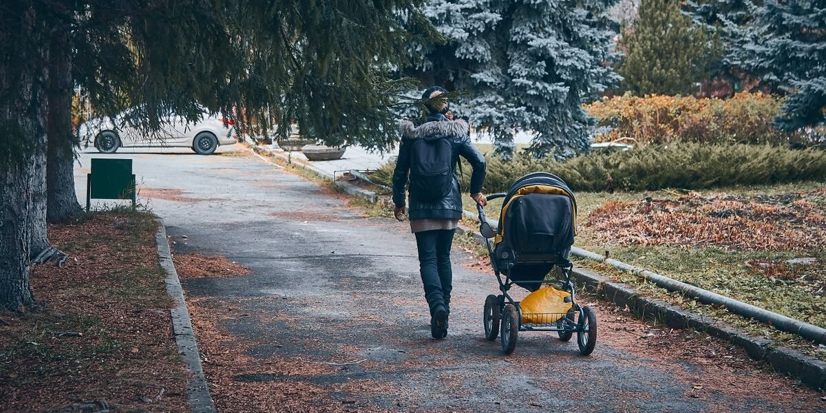 Ouder wandelt met een wandelwagen door het park op een herfstdag.