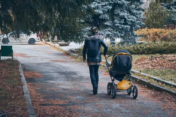 Ouder wandelt met een wandelwagen door het park op een herfstdag.