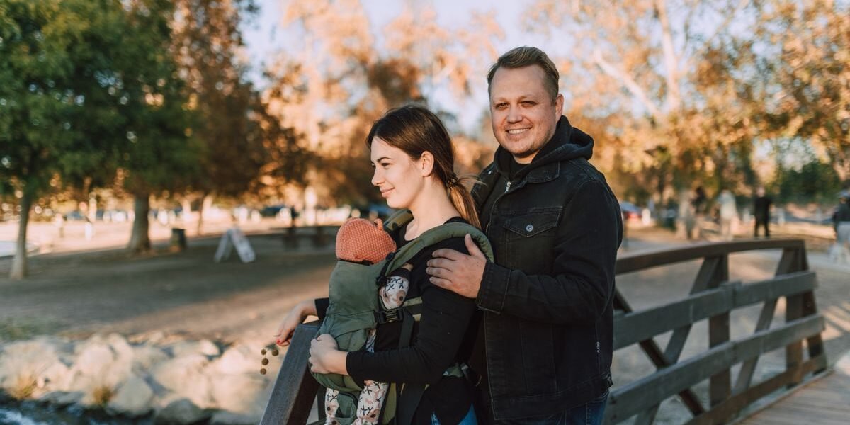 Papa met partner en baby in een verstelbare draagzak in het park