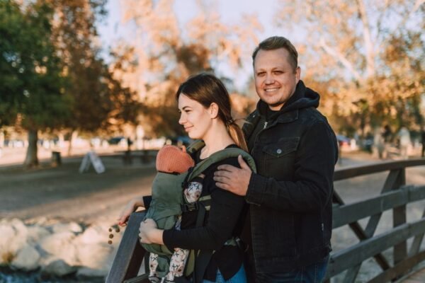Papa met partner en baby in een verstelbare draagzak in het park