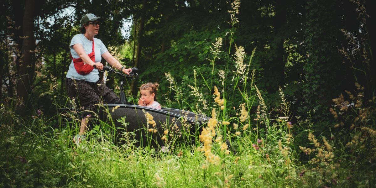 Ouder fietst met kind buiten, thema fietskar voor 2 kinderen