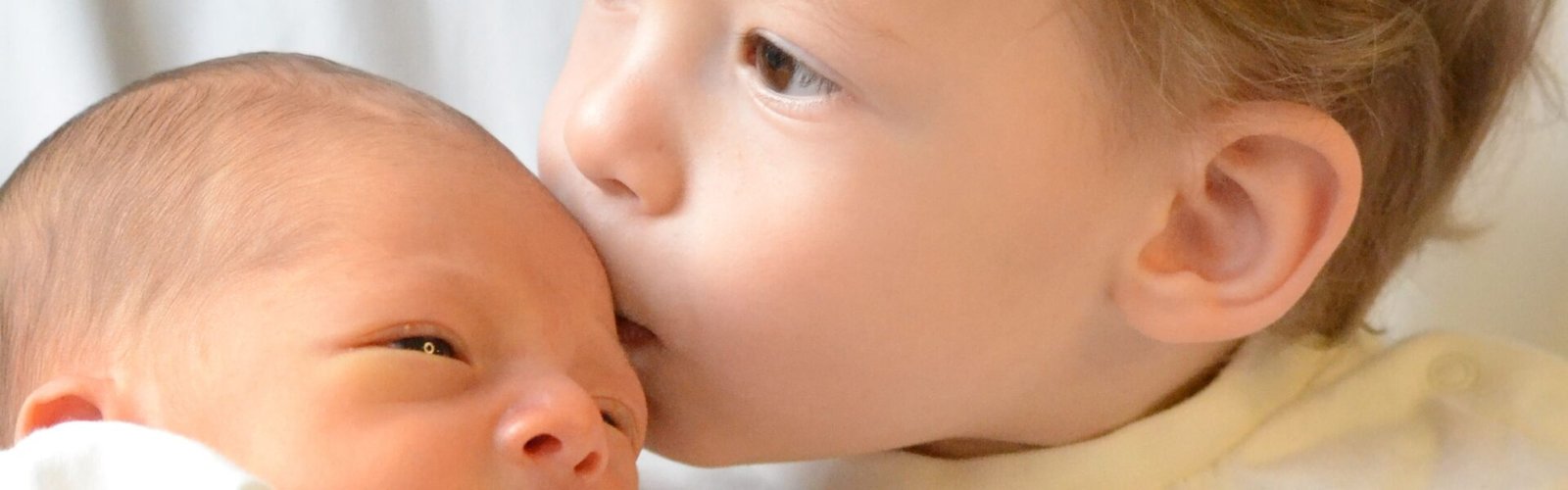 Grote zus geeft pasgeboren baby een kus, kraamcadeau voor tweede kind
