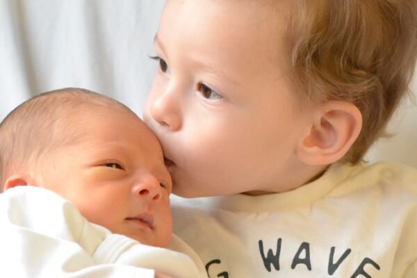 Grote zus geeft pasgeboren baby een kus, kraamcadeau voor tweede kind