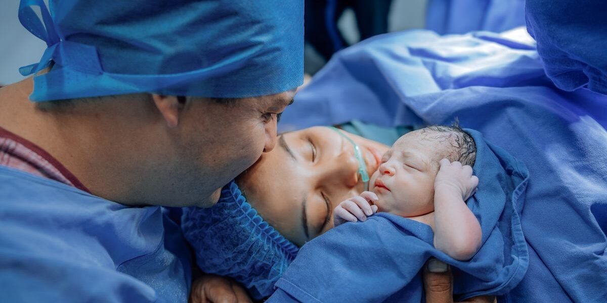 Partner geeft mama een kus na de bevalling terwijl ze de pasgeboren baby vasthoudt in het ziekenhuis