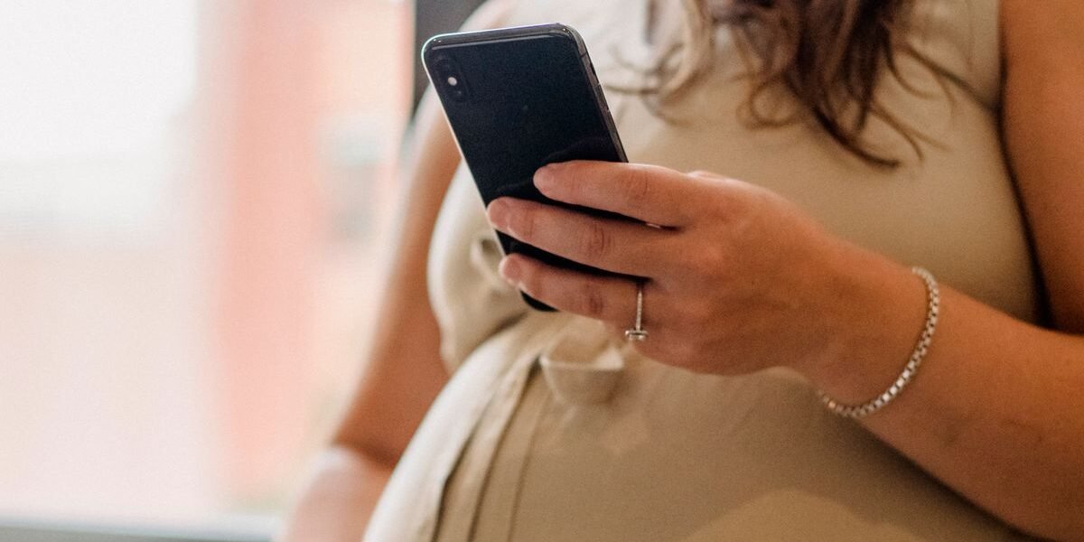Zwangere vrouw typt een adresverzoek voor het geboortekaartje op haar telefoon
