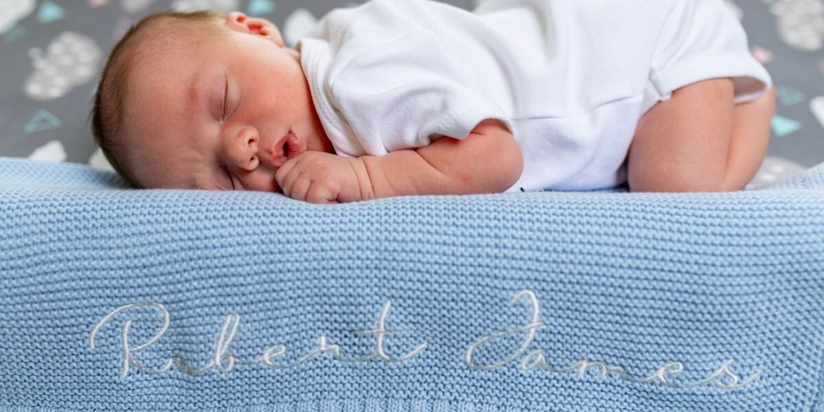 Baby deken met naam geborduurd opgevouwen op wieg