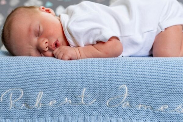Baby deken met naam geborduurd opgevouwen op wieg