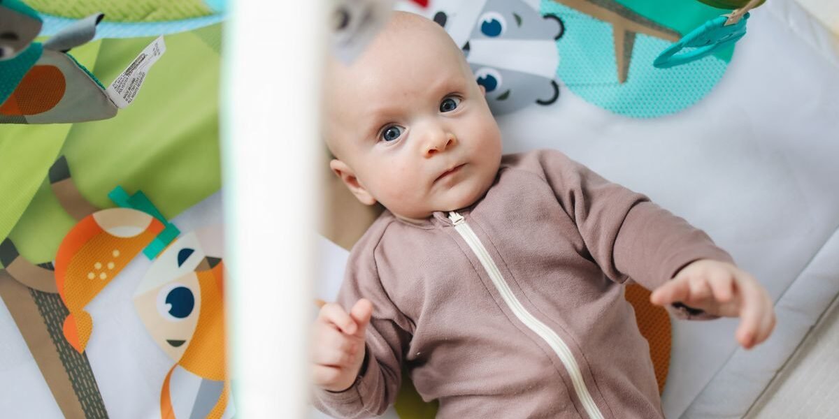 Babyjongen in olijfgroen boxpakje op speelkleed met knuffel