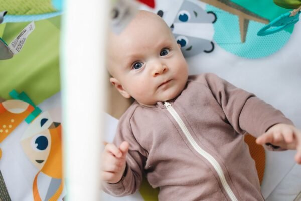 Babyjongen in olijfgroen boxpakje op speelkleed met knuffel