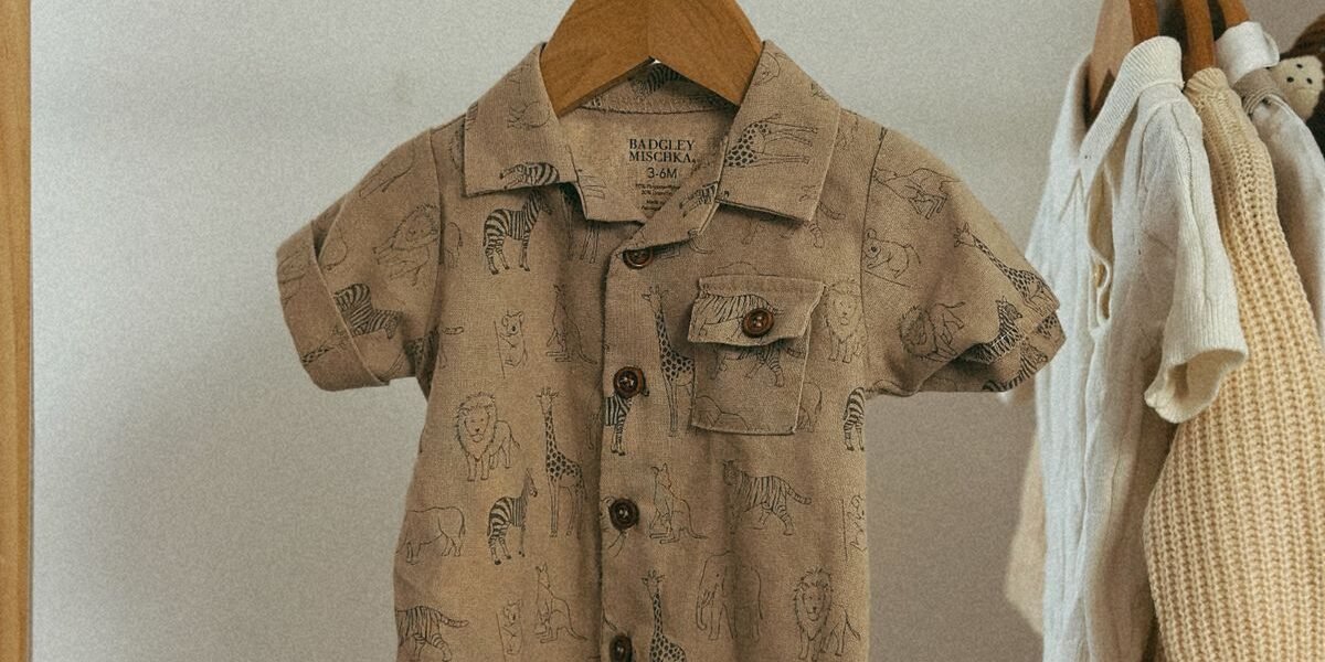 Neutrale babykleding in naturel en zand gestapeld naast houten rammelaar