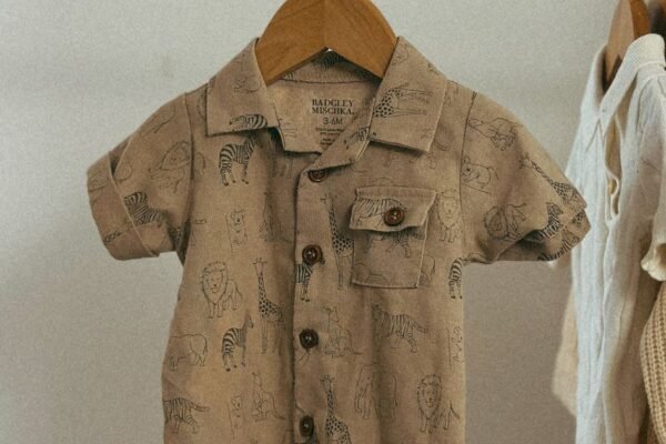Neutrale babykleding in naturel en zand gestapeld naast houten rammelaar