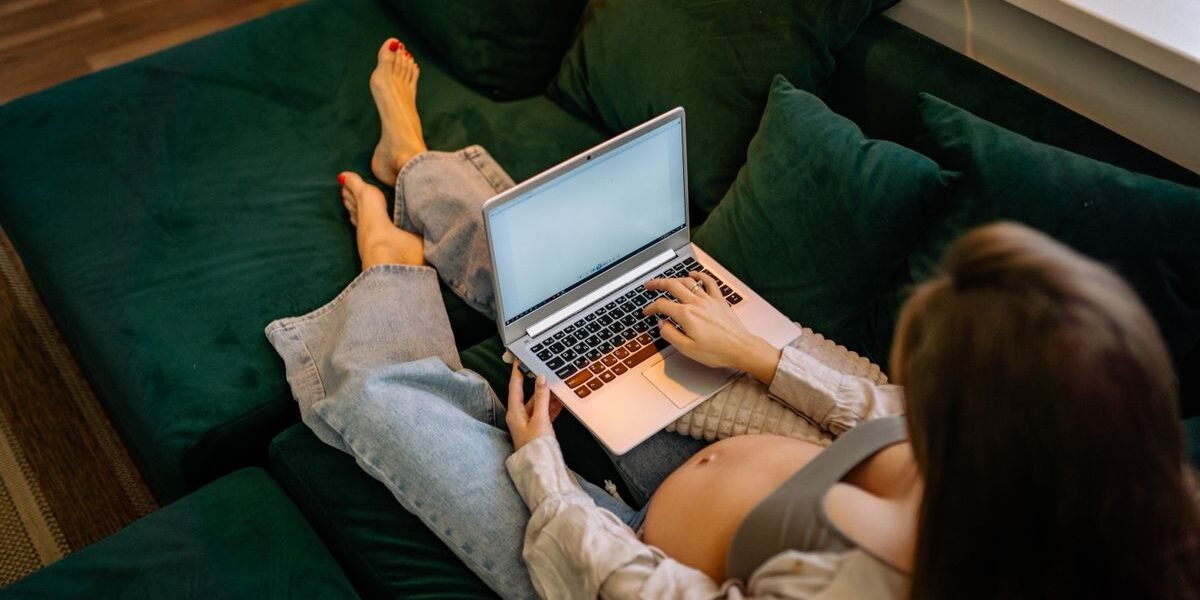 Zwangere vrouw stelt geboortelijst samen met notitieboek en laptop