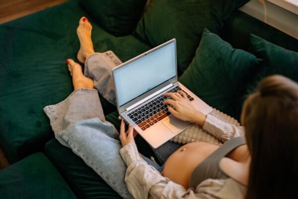 Zwangere vrouw stelt geboortelijst samen met notitieboek en laptop