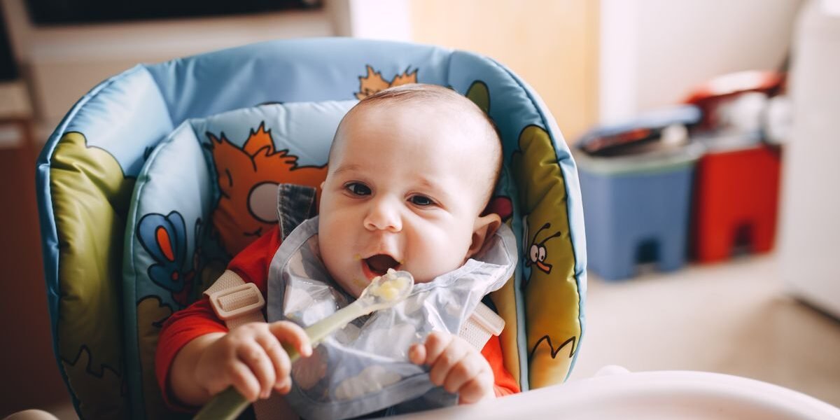 Baby van 6 maanden in kinderstoel eet eerste hapjes met slabbetje