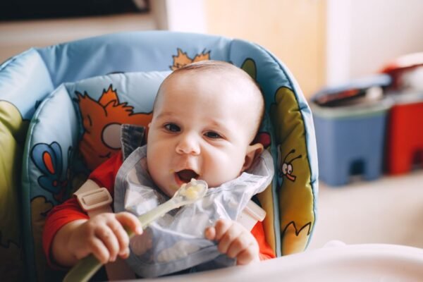 Baby van 6 maanden in kinderstoel eet eerste hapjes met slabbetje