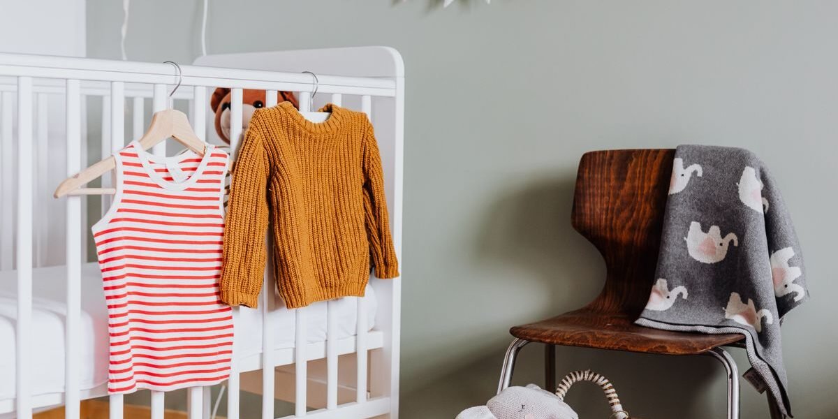 Babykamer zonder kledingkast met kleertjes aan het ledikant gehangen