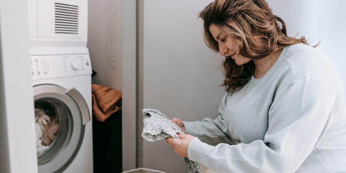 Vrouw zet babykleding in de wasmachine en kiest de temperatuur