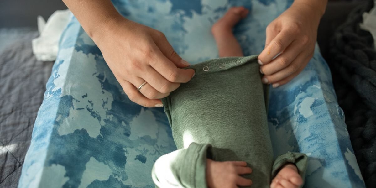 Zwangere vrouw bekijkt rompers voor de babyuitzet op bed