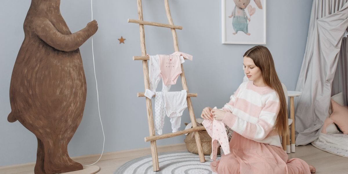 Zwangere vrouw vouwt gewassen babykleding in de babykamer