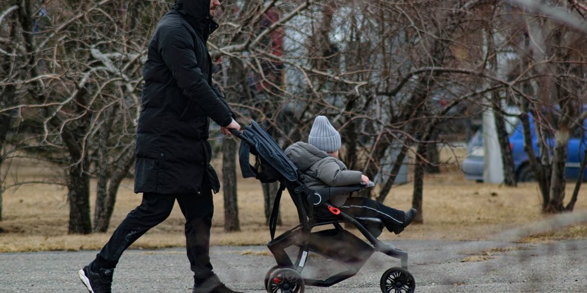 Lange vader duwt kinderwagen in winters park, kinderwagen voor lange mensen
