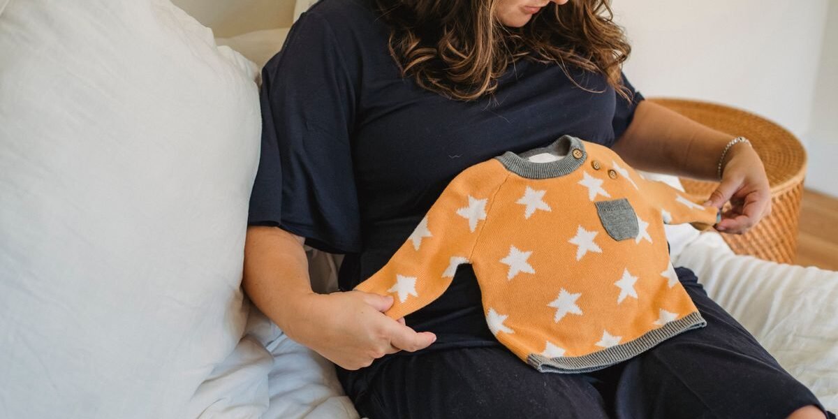 Zwangere vrouw met babykleertjes op bed, klaar voor de ziekenhuistas