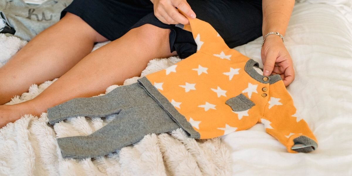 Zwangere vrouw vouwt babykleertjes voor de ziekenhuistas van de bevalling